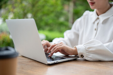 Fototapeta premium Close-up image of a woman typing on laptop keyboard, working on her laptop at a table outdoors.
