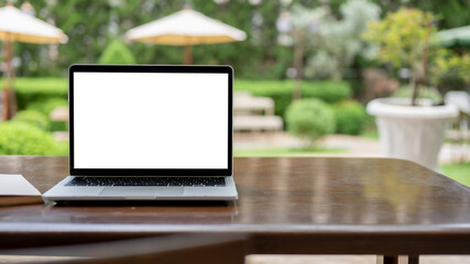 A laptop mockup on a table in a cafe with a blurred beautiful greenery garden in the background.