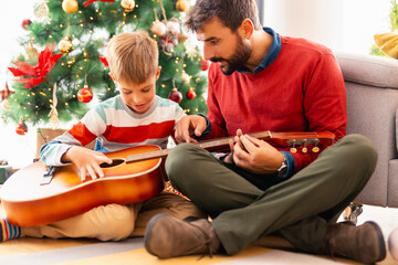 Father teaching son how to play the guitar on Christmas day at home