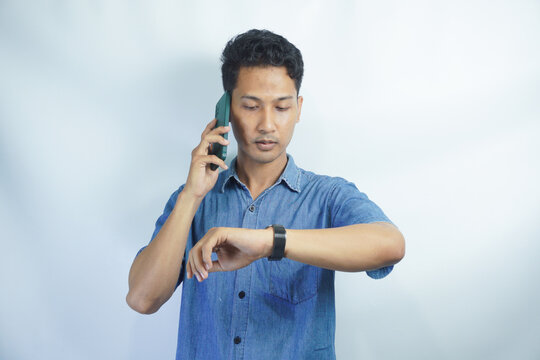 Young Asian Businessman Wearing Blue Shirt Worried Looking At His Watch. Man Is On The Phone And Looking At His Watch