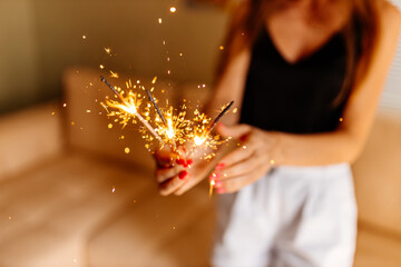A young girl with beautiful well-groomed hands holds burning sparklers. Girl's hands and New Year's...