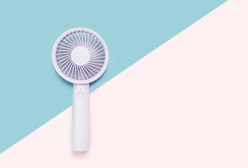 Small portable mini fan on blue and pink background close-up.