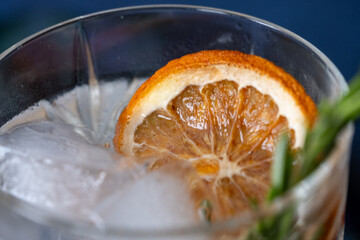 Glass of gin and tonic cocktails with ice, sprig of rosemary and sliced dry orange on a blue background. Copy space