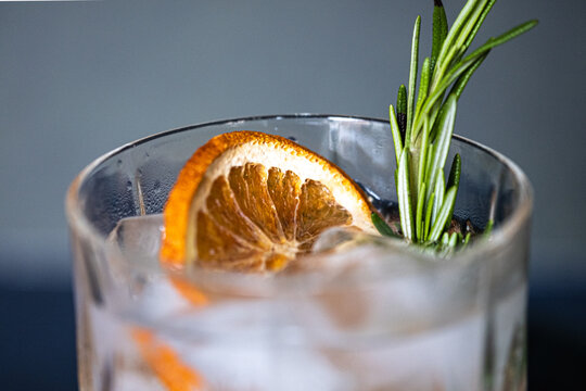 Glass of gin and tonic cocktails with ice, sprig of rosemary and sliced dry orange on a blue background. Copy space