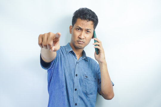 Young Asian Man is angry and pointing when calling in the phone. Indonesian man wearing a blue shirt.