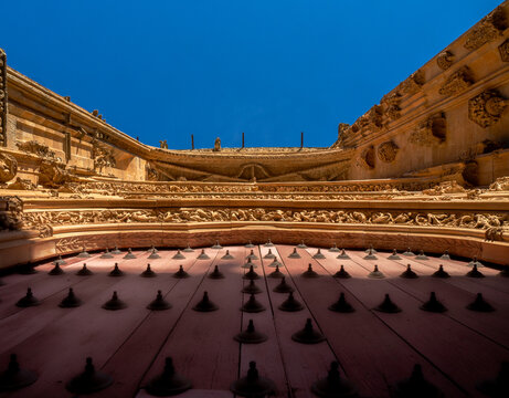Detailed view from below of the ornaments on the main red wooden door with wrought iron motifs and the cornice with gargoyles of the New Cathedral of Salamanca illuminated by the evening light