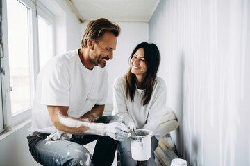 Fototapeta premium Happy newlyweds hug and rejoice after moving into a new house by taking out a mortgage. A couple in love make repairs together in an empty bright interior in an apartment. Selective focus.