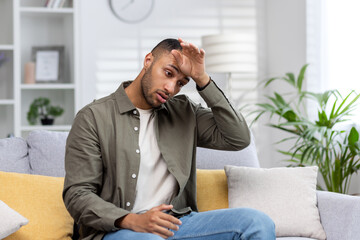 Portrait of a blond hispanic man sitting on the sofa at home and holding his hand above his head...