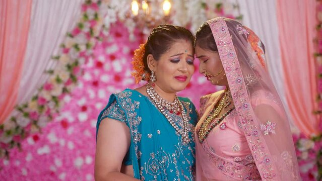 Sad Mother crying by hugging bride daughter during marriage ceremony on stage - concept of emotional farewell, family bonding and Unconditional Love.