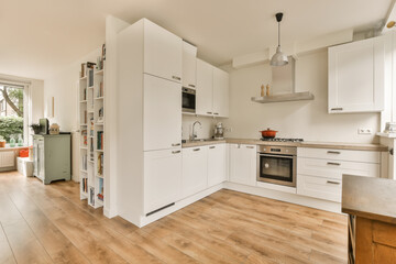 a kitchen with wood flooring and white cabinets in the middle part of the room, there is an oven on the right side