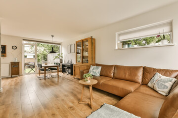 a living room with wood flooring and brown leather couches in the center of the room is an open kitchen, dining area