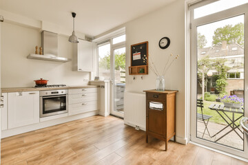 a kitchen with wood flooring and white cabinetd doors leading to an open patio door that leads out onto the back yard