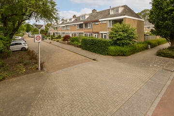 a street with houses in the background and trees on either side, some cars are parked near each other buildings