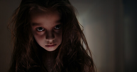 Portrait of an angry ghost girl with black hair staring intently at the camera. Powerful low key image of little girl in dark side with shadow on face with blissful eyes looking up. Halloween.
