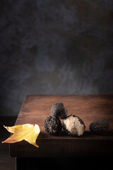 Black mushrooms truffles in antique wooden board with autumn leaves, rustic style, low key,...