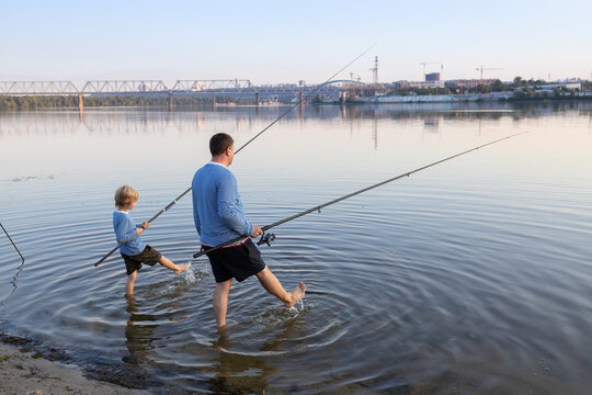 father's day concept. Dad and son go fishing together, stand in the water with fishing rods and merrily splash with their feet. Family interesting pastime for the weekend. Hobby of child and parent