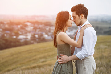 Sun rays fall on man and woman in love hugging on hill top overlooking city. Concept of scenic view and couple photoshoot. Beauty of nature and lovers
