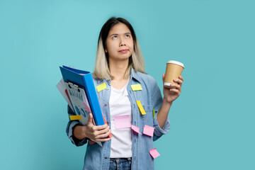 Asian female office worker is bored with a lot of paperwork at hand. She looks up, standing isolated on a pastel blue background.