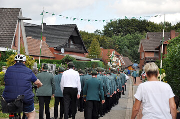 Schützenfest ist: Schützen in Uniform marschieren durch die Siedlung zum Schützenplatz, von hinten fotografiert.