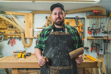 Portrait of caucasian carpenter with tools in both hands standing inside his workshop . High quality photo
