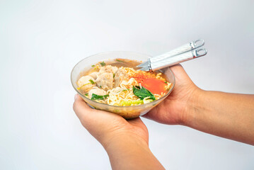 A human hand holding a bowl with a meatball (bakso)