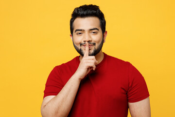 Young secret fun happy Indian man he wears red t-shirt casual clothes say hush be quiet with finger...