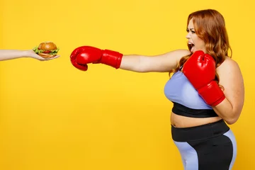 Fototapete Graffiti-Collage Young chubby overweight plus size big fat fit woman wear blue top red gloves warm up training boxing against fast food burger isolated on plain yellow background studio home gym Workout sport concept