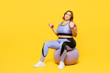 Obraz premium Full body young sad chubby plus size big fat fit woman wear blue top warm up train sit on fit ball hold dumbbells look camera isolated on plain yellow background studio home gym Workout sport concept