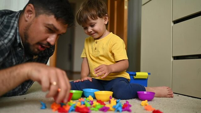 A father and son are sorting colorful toys into matching bowls, promoting organization and color identification abilities