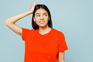 Young confused minded pensive latin woman wear orange red t-shirt casual clothes look aside on area scratch head isolated on plain pastel light blue cyan background studio portrait. Lifestyle concept.