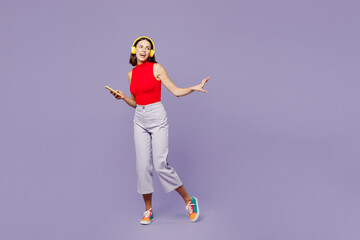 Fototapeta na wymiar Full body young woman she wears red tank shirt casual clothes listen ot music in headphones use mobile cell phone isolated on plain pastel light purple background studio portrait. Lifestyle concept.