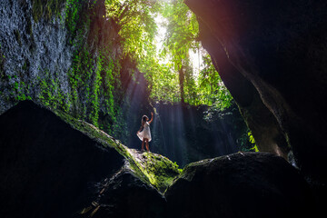 Fototapeta na wymiar Young woman tourism with rays of light enjoying Tukad Cepung Waterfall at Bali, Indonesia