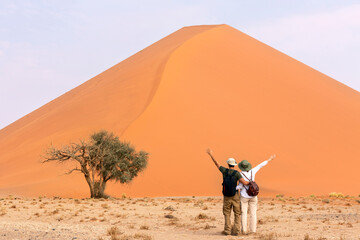 couple travelers standing  near orange sand dune with open arms. Travel desert concept