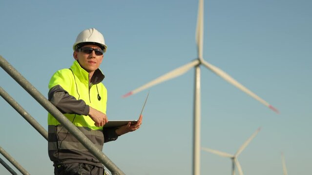 Engineer with a laptop stands on the stairs of a wind turbine