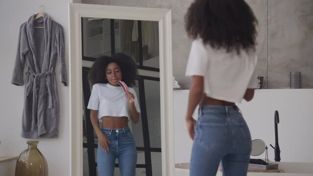 Black Woman Singing in Hairbrush as Microphone. Cheerful African American female dancing in bathroom looking in the mirror.