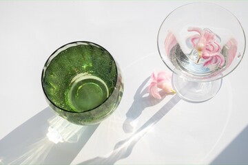 green glass cup with water and a container with spring flowers. Abstract shadow pattern on a white background. View from above.