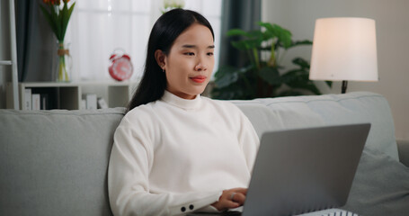 Asian woman using a laptop computer while sitting on the sofa
