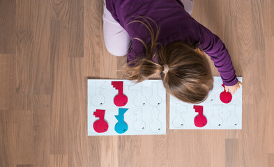 Little girl plays an educational game at home. Preschooler learns shapes indoors. Homeschooling concept.