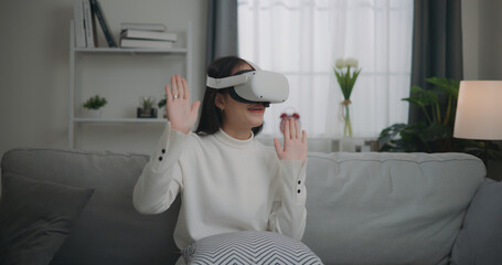 Asian woman watching a concert via VR glasses and dancing while sitting on the sofa
