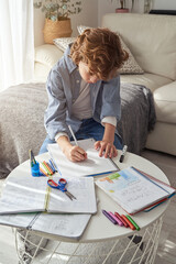 Preteen boy sitting on corner of sofa and drawing on paper