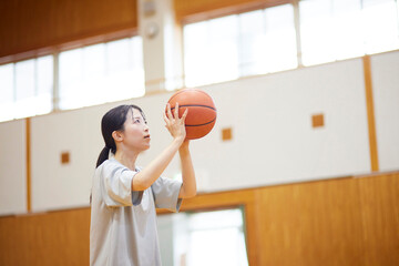 体育館でバスケットボールの練習をするスポーツウェアを着た日本人女性