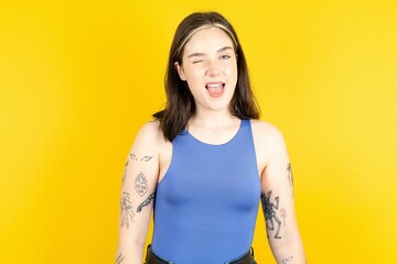 Coquettish Beautiful woman wearing blue tank top smiling happily, blinking at camera in a playful...