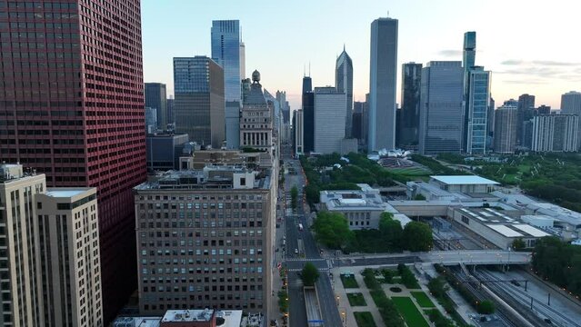 Michigan Avenue in downtown Chicago, Illinois. Aerial truck shot revealing park, skyline from behind skyscrapers. Beautiful drone shot during sunrise. Millenium Park, the Bean, and the Art Institute.