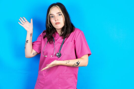 Young caucasian doctor woman wearing pink medical uniform pointing aside with both hands showing something strange and saying: I don't know what is this. Advertisement concept.