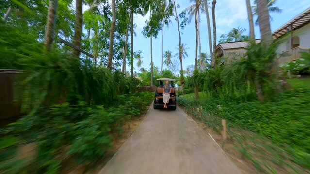 FPV drone following woman in a golf cart on a tropical vacation.