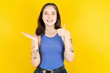 Beautiful woman wearing blue tank top Showing palm hand and doing ok gesture with thumbs up,...