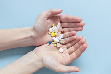 Woman holding pills in two hands taking emergency medicine, supplements or antibiotic antidepressant painkiller medication to relieve pain, meds side effects concept, close up on blue background..