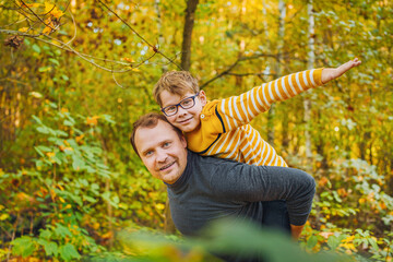  Son and father with autumn leaves in the yellow autumn park.