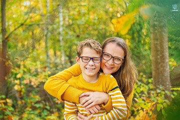 Fototapeta premium Mother and son and with autumn leaves have fun in the yellow autumn park.