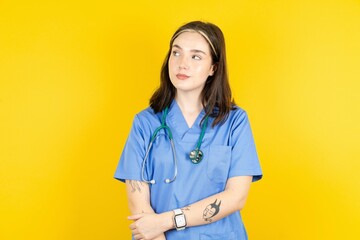 Pleased Young caucasian doctor woman wearing blue medical uniform keeps hands crossed over chest looks happily aside